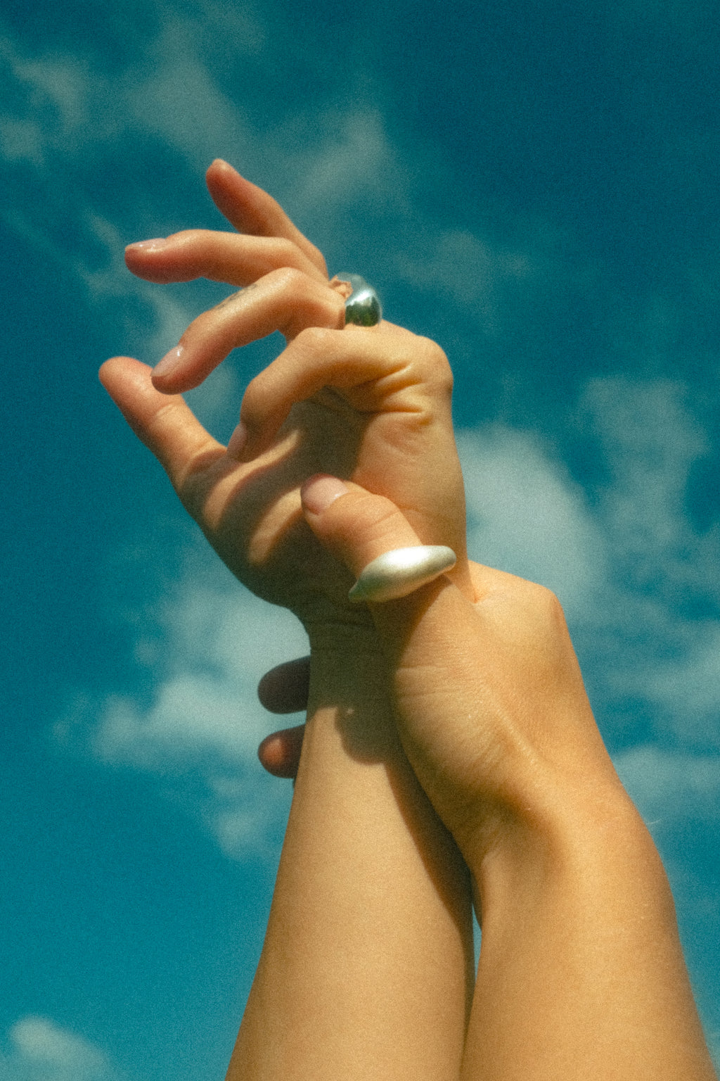 Two hands with rings against a blue sky