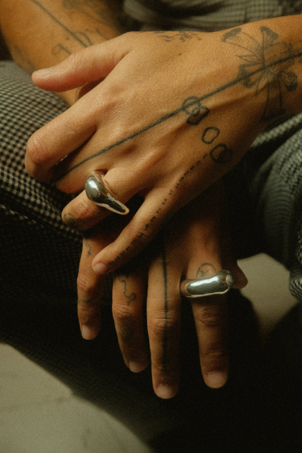 Close-up of tattooed hands with silver rings on a dark background