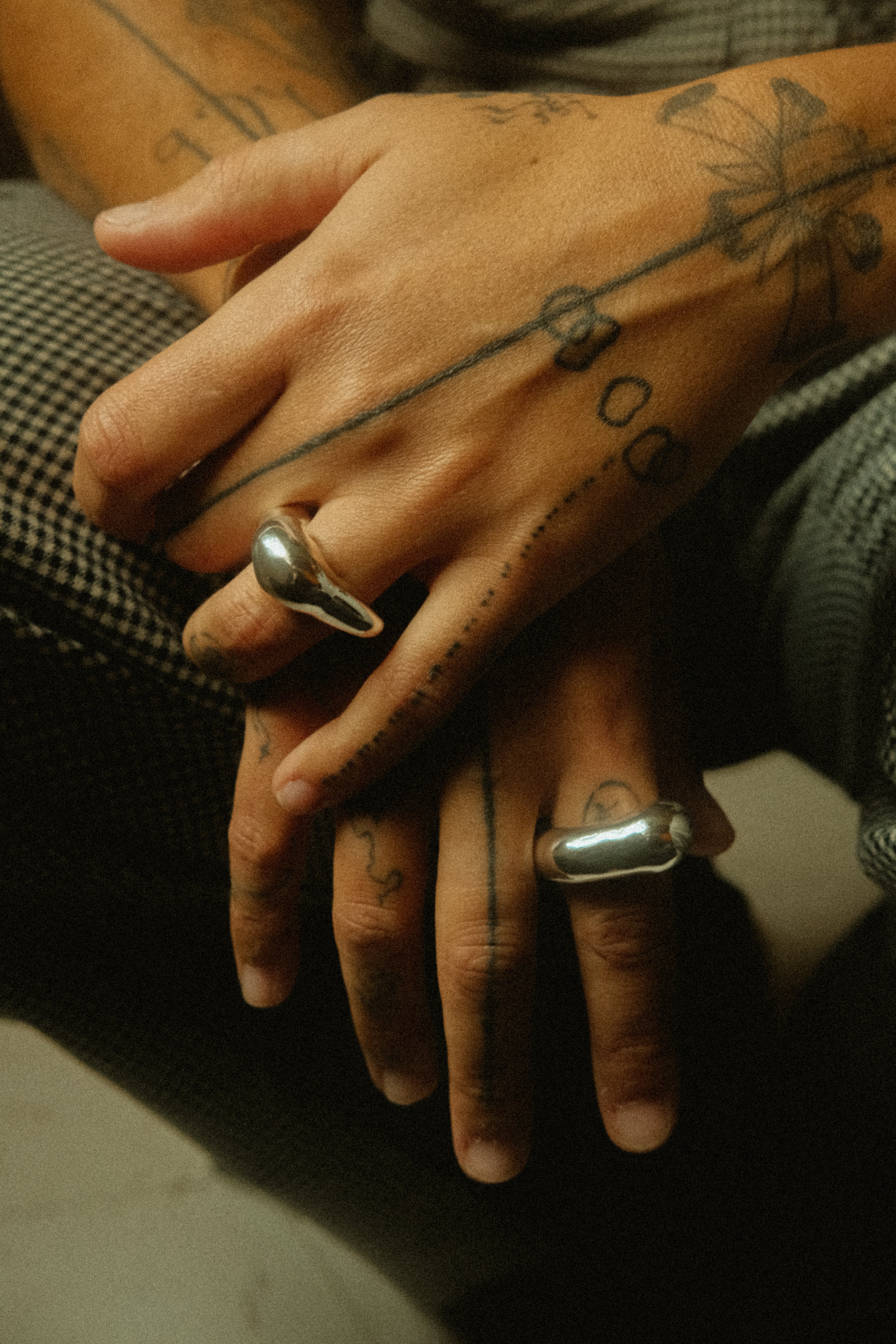 Close-up of tattooed hands with silver rings on a dark background